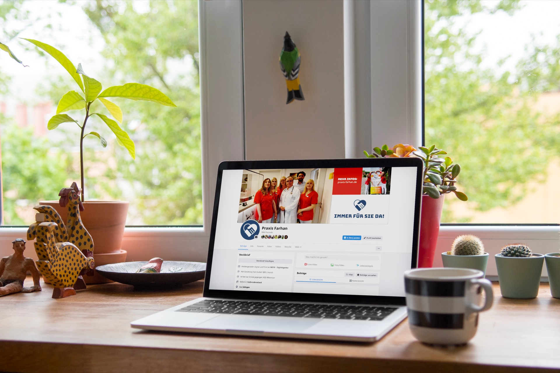 Laptop auf einem Holztisch am Fenster mit dem Social-Media-Auftritt der Hausarztpraxis Dr. Farhan in Aurich