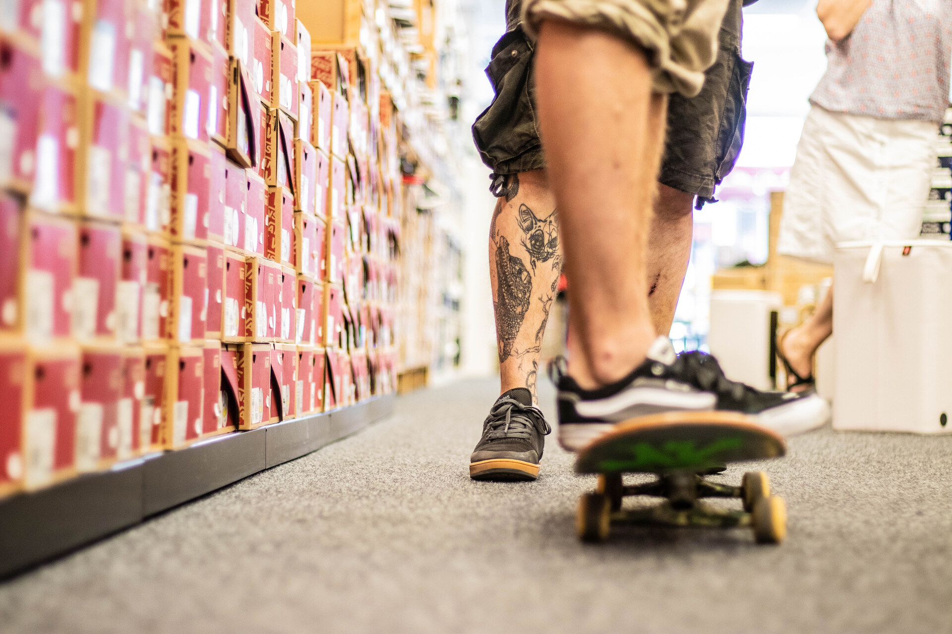 Skater rollt im Laden der Sportschuh-Börse Aurich auf dem Skateboard durch den Gang zwischen deckenhohen Stapeln roter Schuhkartons