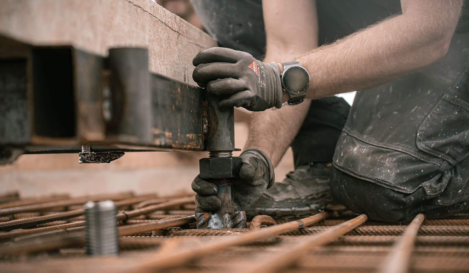 Betonbauer von Moorkamp Bau zieht mit Arbeitshandschuhen eine schwere Spindelmutter an der Schalung über dem Bewehrungsstahl fest