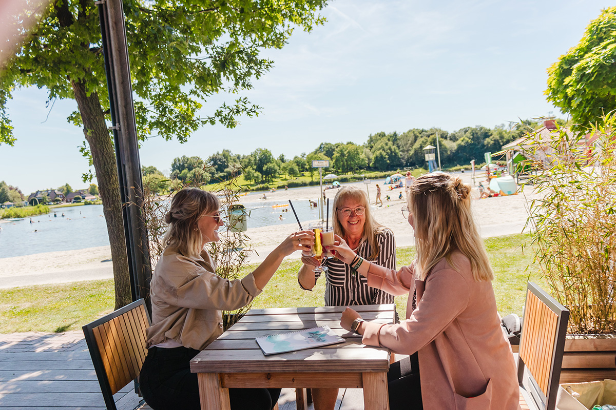 Urlaubsgäste stoßen am Badesee Ihler Meer in der Gemeinde Ihlow an – auf dem Tisch liegt das von m01n gestaltete Urlaubsmagazin
