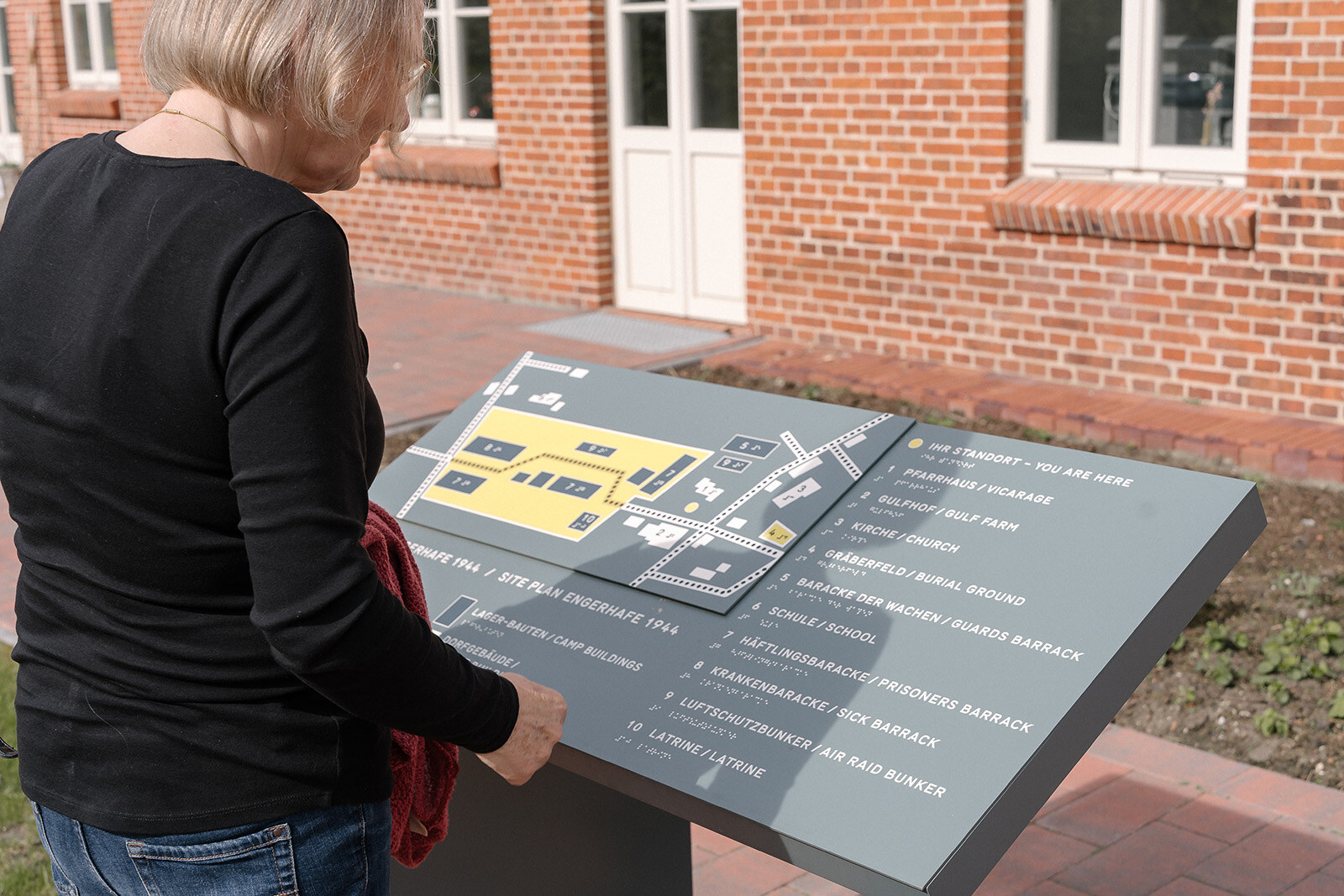 Besucherin am ertastbaren Bronzelageplan mit Blindenschrift der KZ-Gedenkstätte Engerhafe